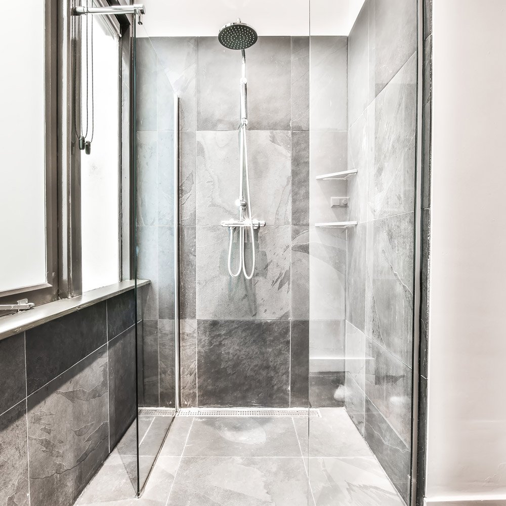Glass-walled shower with a large rainfall head and handheld sprayer on gray tiled wall.